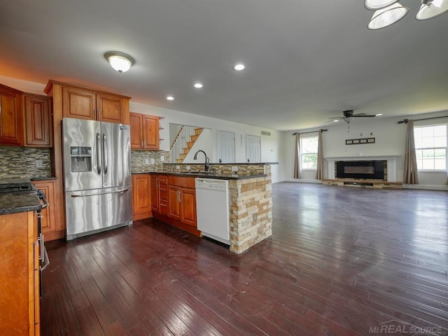 kitchen featuring appliances with stainless steel finishes, brown cabinets, open floor plan, a peninsula, and a healthy amount of sunlight