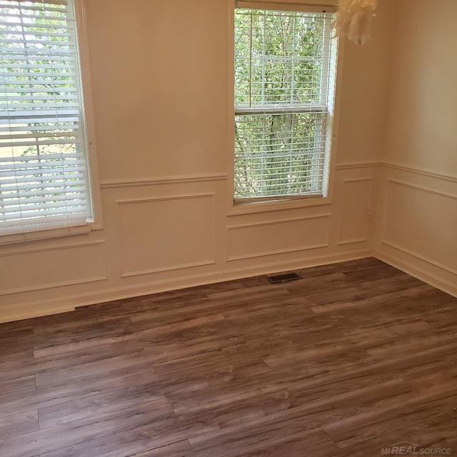 unfurnished room featuring dark wood-type flooring, wainscoting, a wealth of natural light, and a decorative wall