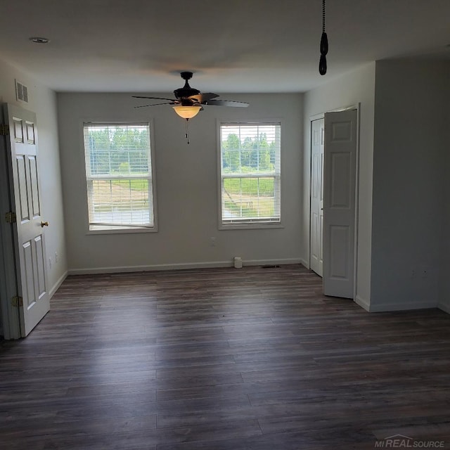 unfurnished room with ceiling fan, dark wood finished floors, visible vents, and baseboards