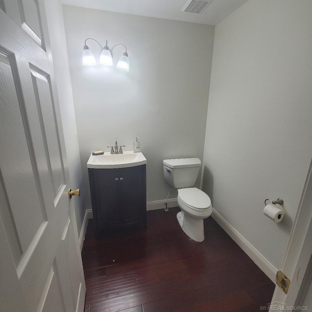 half bath with toilet, wood finished floors, visible vents, vanity, and baseboards