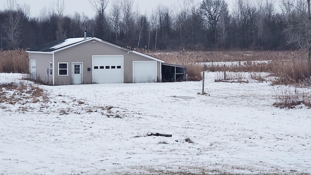 snow covered garage featuring a detached garage and a forest view