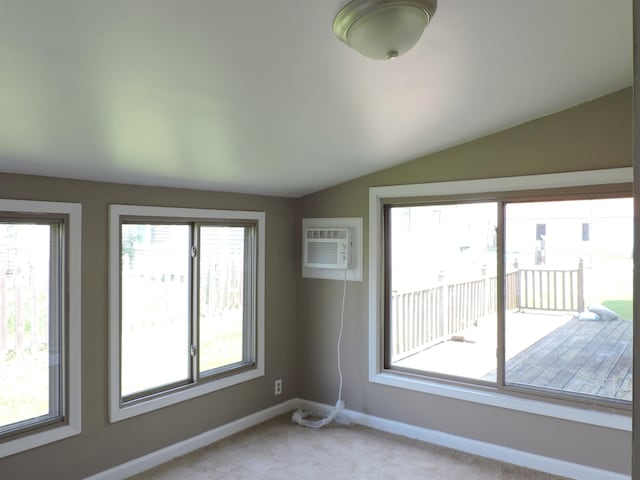 carpeted spare room featuring a wall mounted air conditioner, a healthy amount of sunlight, and vaulted ceiling