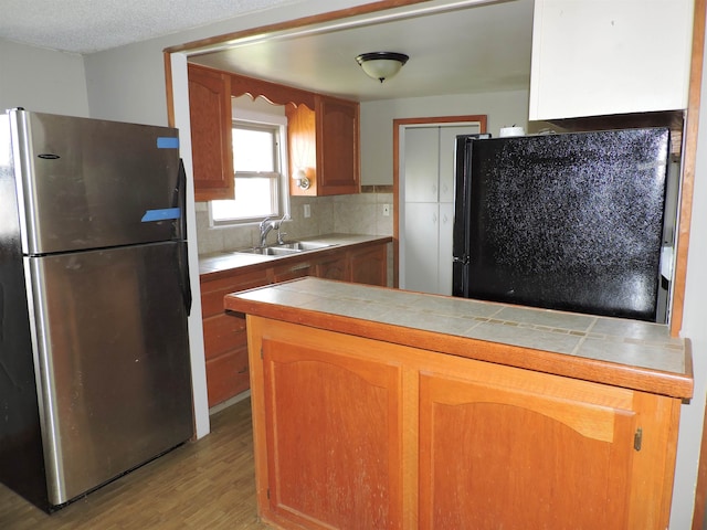 kitchen with sink, stainless steel refrigerator, tile countertops, and light hardwood / wood-style floors