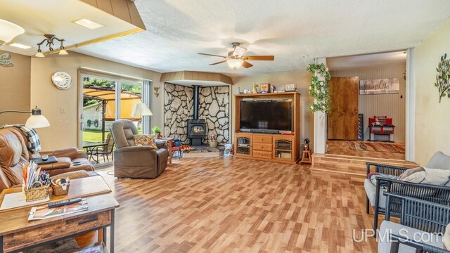 living room with a textured ceiling, ceiling fan, wood-type flooring, and a wood stove