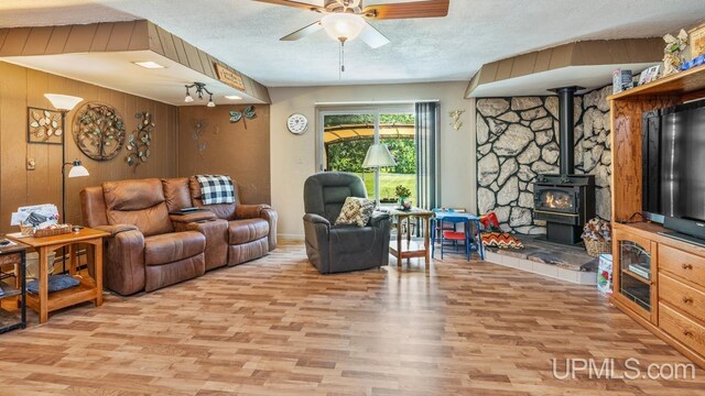 living room with a wood stove, a textured ceiling, wood walls, ceiling fan, and hardwood / wood-style floors