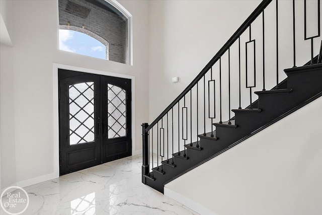 foyer with baseboards, a towering ceiling, marble finish floor, stairs, and french doors