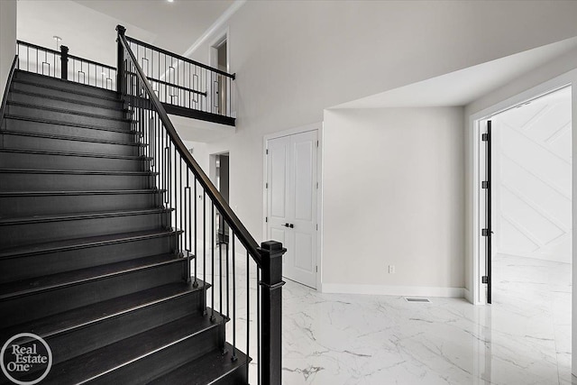 staircase with a towering ceiling, marble finish floor, and baseboards