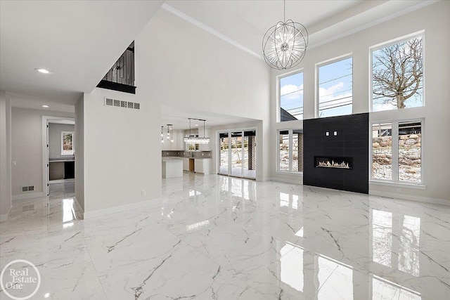 unfurnished living room with a warm lit fireplace, marble finish floor, visible vents, and an inviting chandelier