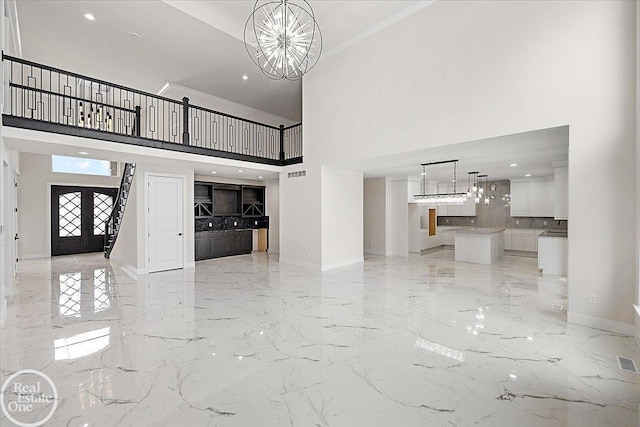 foyer entrance with crown molding, a towering ceiling, an inviting chandelier, and french doors