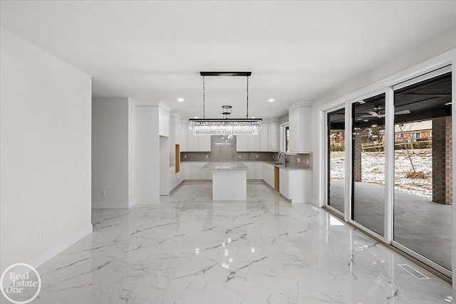 kitchen featuring a sink, a center island, white cabinets, marble finish floor, and decorative backsplash