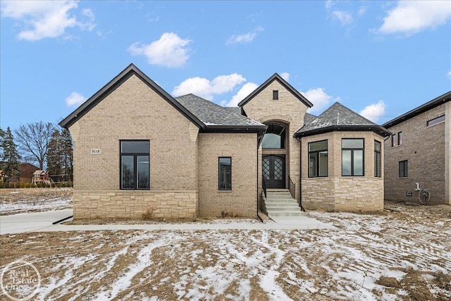 french country style house featuring stone siding, brick siding, and roof with shingles