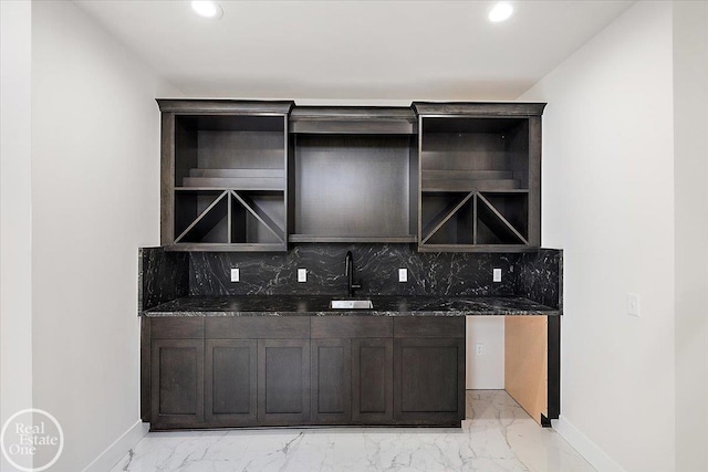 bar with dark brown cabinetry, dark stone counters, sink, and backsplash