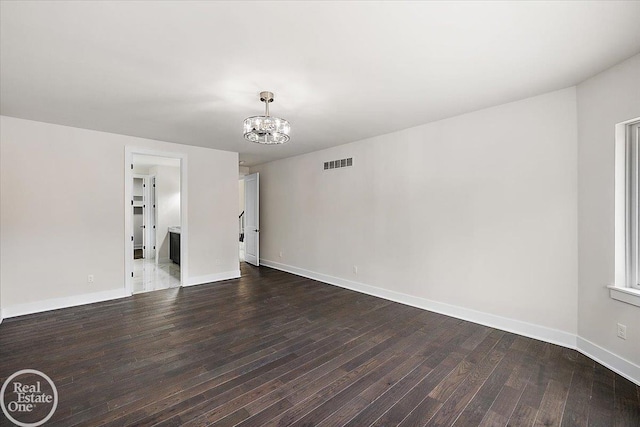 spare room featuring wood-type flooring, visible vents, a chandelier, and baseboards