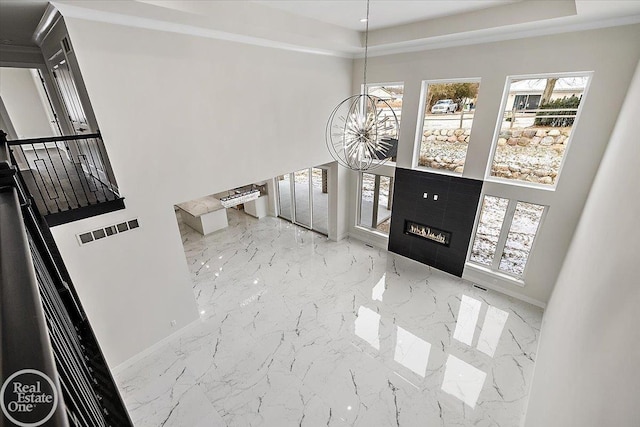 foyer with a notable chandelier, visible vents, baseboards, marble finish floor, and a glass covered fireplace