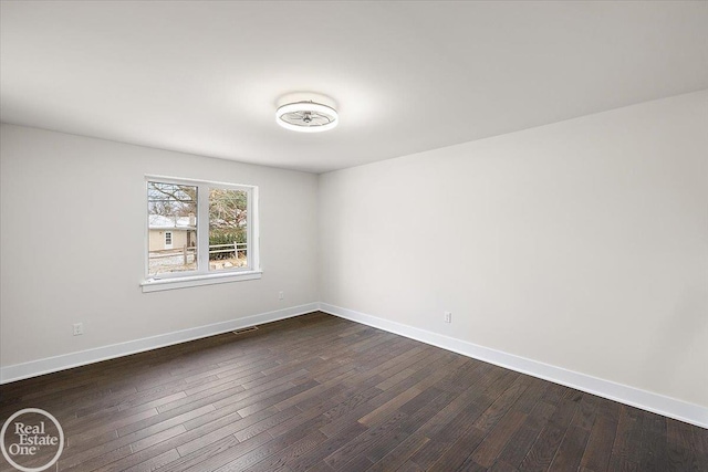 unfurnished room featuring dark wood-style flooring, visible vents, and baseboards