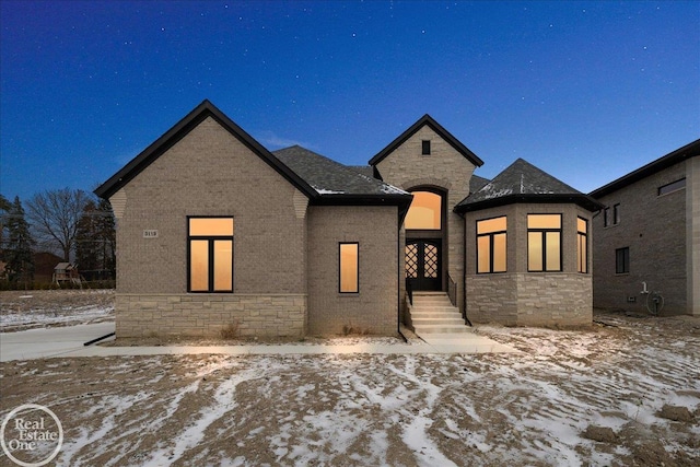 french country inspired facade featuring stone siding, brick siding, and roof with shingles