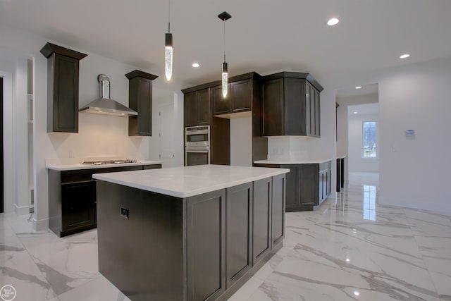 kitchen with appliances with stainless steel finishes, hanging light fixtures, dark brown cabinets, a center island, and wall chimney exhaust hood