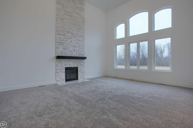 unfurnished living room featuring baseboards, carpet floors, a high ceiling, and a stone fireplace