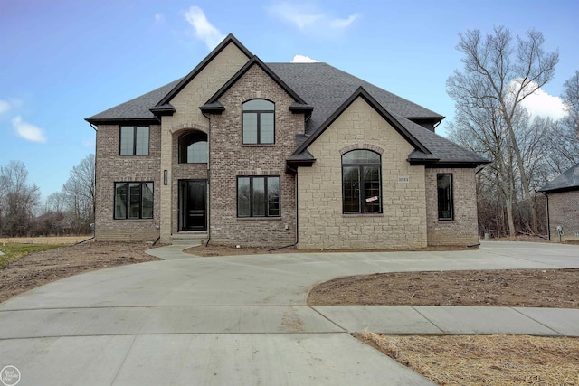 french country style house featuring concrete driveway, brick siding, and a shingled roof