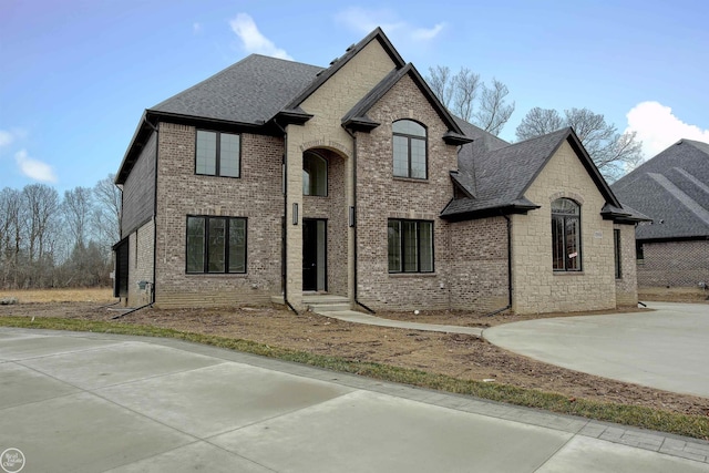 french country inspired facade with stone siding, brick siding, and roof with shingles