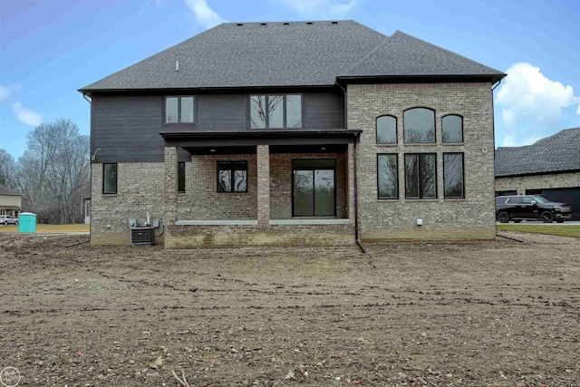 rear view of house featuring brick siding, central AC unit, and a shingled roof