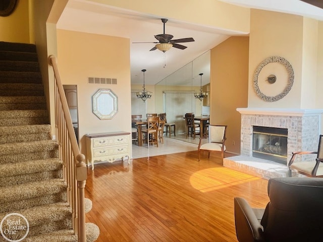 living room featuring visible vents, stairs, vaulted ceiling, ceiling fan with notable chandelier, and wood finished floors