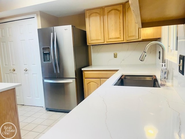 kitchen with tasteful backsplash, light stone countertops, light tile patterned flooring, stainless steel fridge, and a sink