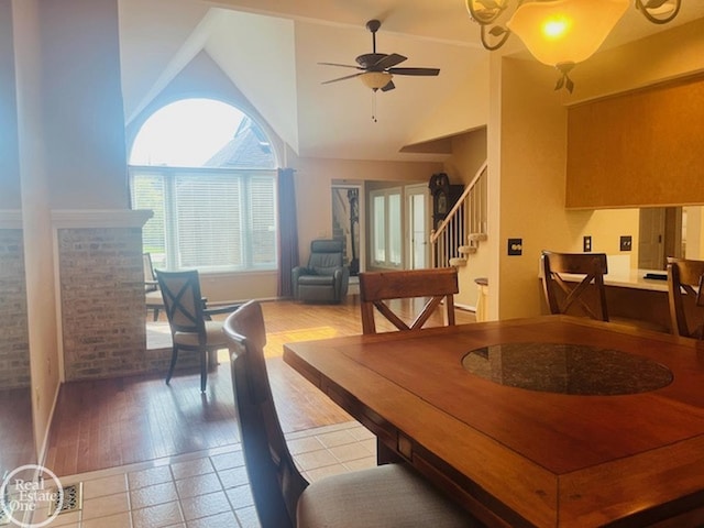 dining area featuring light wood-type flooring, high vaulted ceiling, stairs, and a ceiling fan