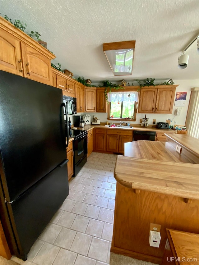 kitchen featuring light tile patterned flooring, black appliances, butcher block counters, and a textured ceiling