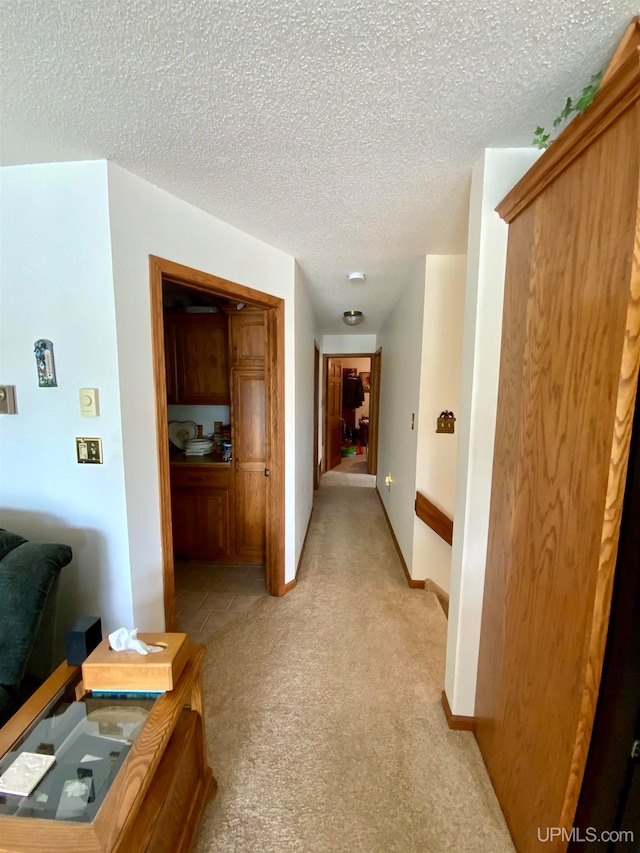 hallway with a textured ceiling and light carpet