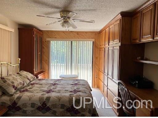 bedroom with ceiling fan, wood walls, and a textured ceiling