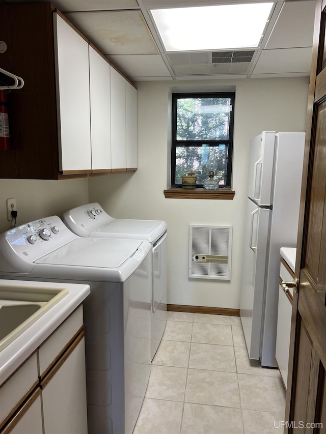 laundry room featuring heating unit, baseboards, washing machine and clothes dryer, cabinet space, and light tile patterned floors