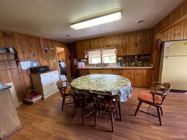 kitchen featuring sink, kitchen peninsula, wood-type flooring, wooden walls, and white fridge