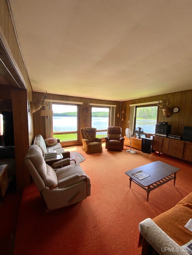 living room with a water view, wooden walls, a healthy amount of sunlight, and carpet flooring