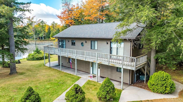 rear view of house with a patio area, a wooden deck, a yard, and roof with shingles