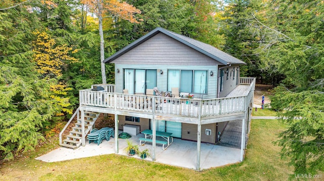 rear view of house featuring a forest view, a wooden deck, a patio area, a yard, and stairs