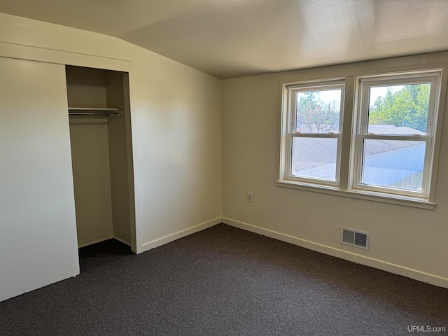 unfurnished bedroom featuring lofted ceiling, dark colored carpet, and a closet