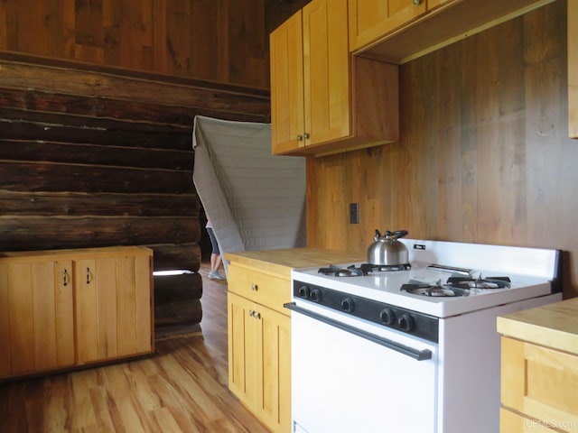 kitchen featuring white gas stove, wood walls, light hardwood / wood-style floors, and light brown cabinets