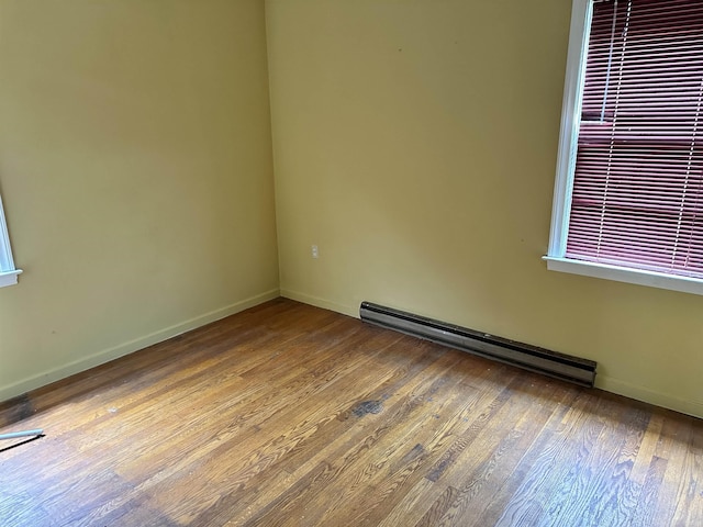 empty room featuring baseboard heating, visible vents, baseboards, and wood-type flooring