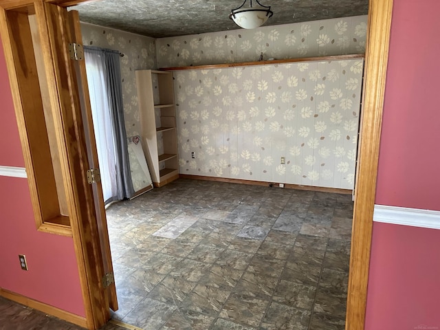 unfurnished room with wallpapered walls and baseboards