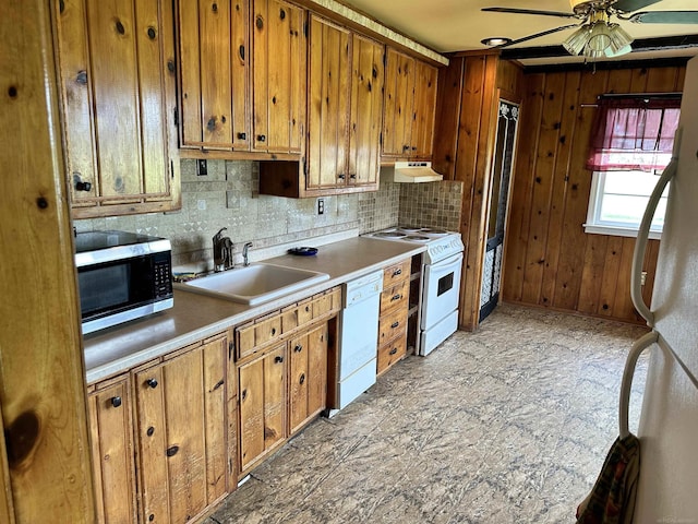 kitchen with white appliances, a ceiling fan, brown cabinetry, a sink, and under cabinet range hood