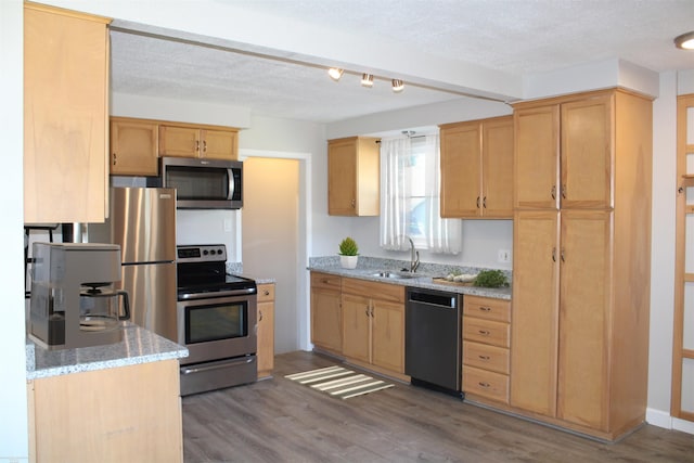 kitchen with light wood-type flooring, a textured ceiling, light stone countertops, appliances with stainless steel finishes, and sink