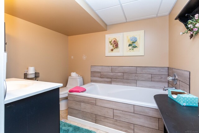 bathroom featuring tile patterned flooring, toilet, vanity, a paneled ceiling, and a relaxing tiled tub