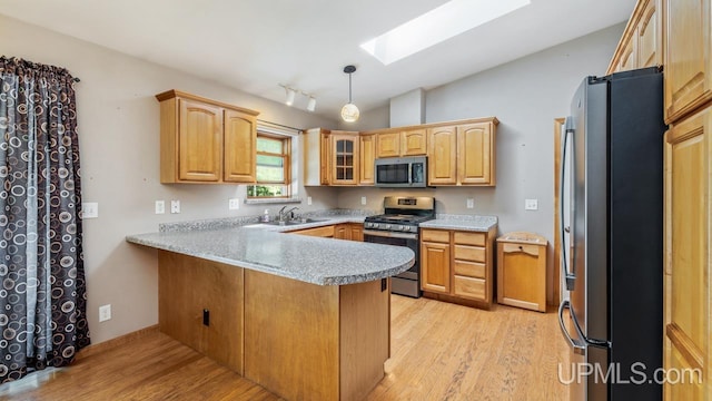 kitchen featuring lofted ceiling with skylight, light wood-type flooring, kitchen peninsula, appliances with stainless steel finishes, and sink