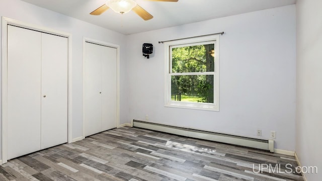 unfurnished bedroom featuring multiple closets, ceiling fan, a baseboard heating unit, and wood-type flooring