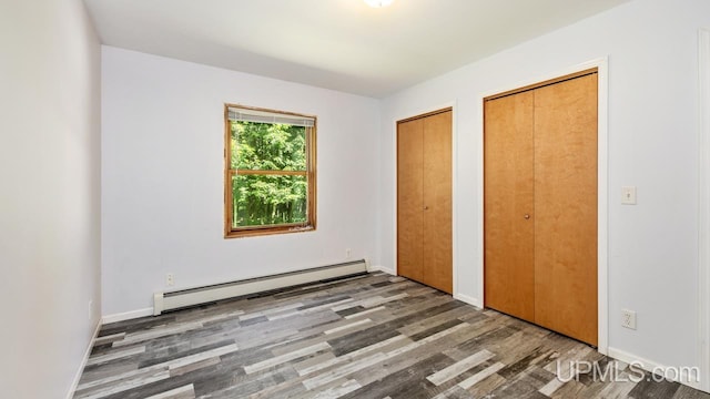 unfurnished bedroom with wood-type flooring, a baseboard radiator, and two closets