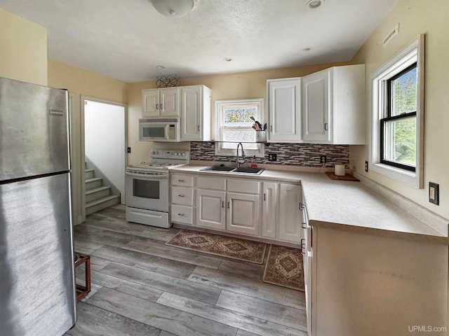 kitchen featuring white cabinets, white appliances, light wood-type flooring, tasteful backsplash, and sink