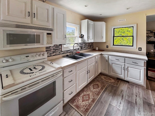 kitchen with white appliances, backsplash, white cabinetry, sink, and hardwood / wood-style floors