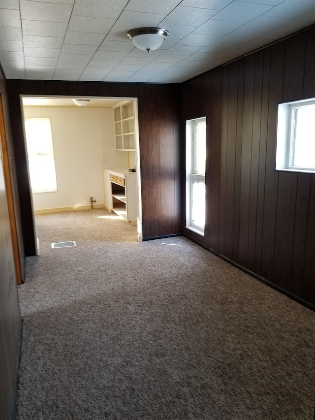 spare room featuring wood walls, carpet flooring, visible vents, and a wealth of natural light