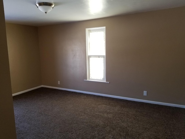spare room with dark carpet and baseboards